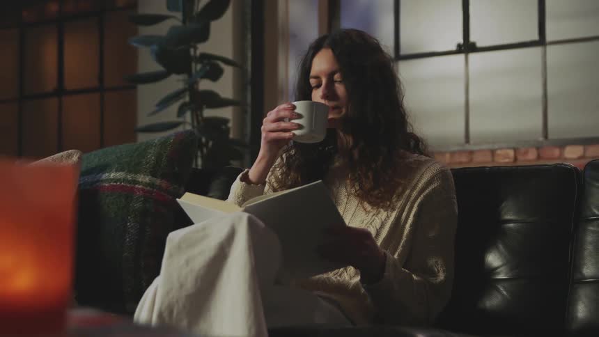 A woman drinks and reads at home