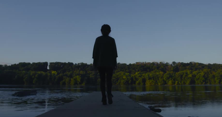 The silhouette of a woman walking along a pier on a lake during the day