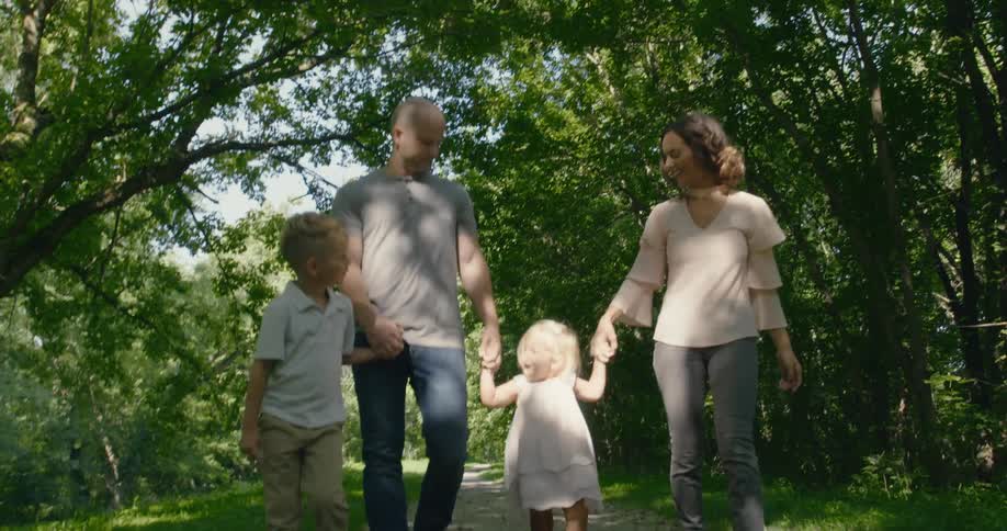 Parents walk along trail through forest park holding their childrens hands