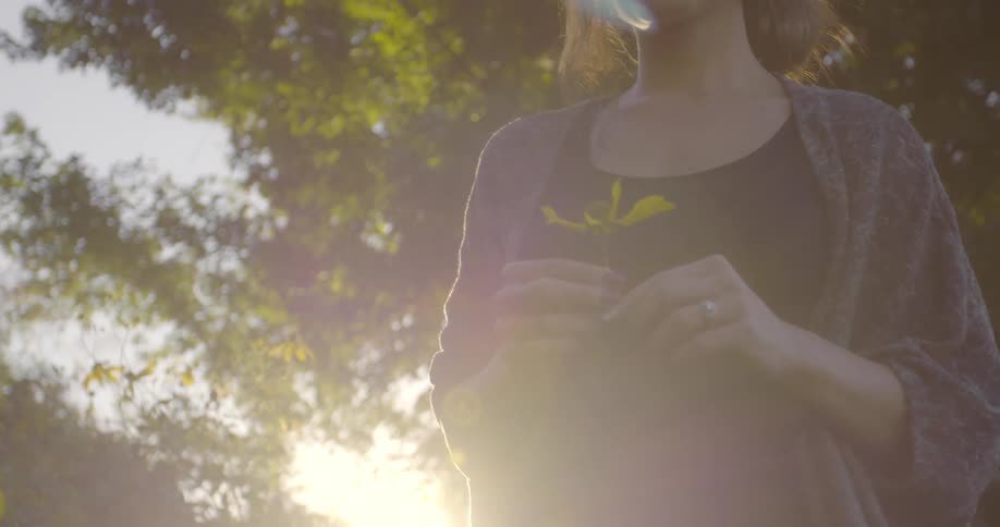 A woman twirls a plant in her hands while walking outdoors during the day