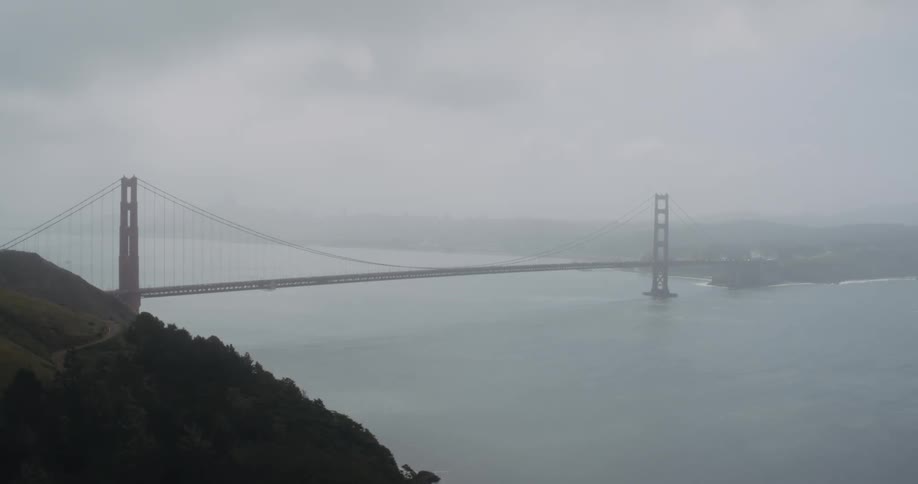 A suspension bridge stretches across the water through the fog