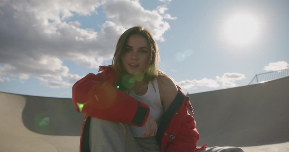 A teenage girl is sitting on a skateboard in a skateboard park