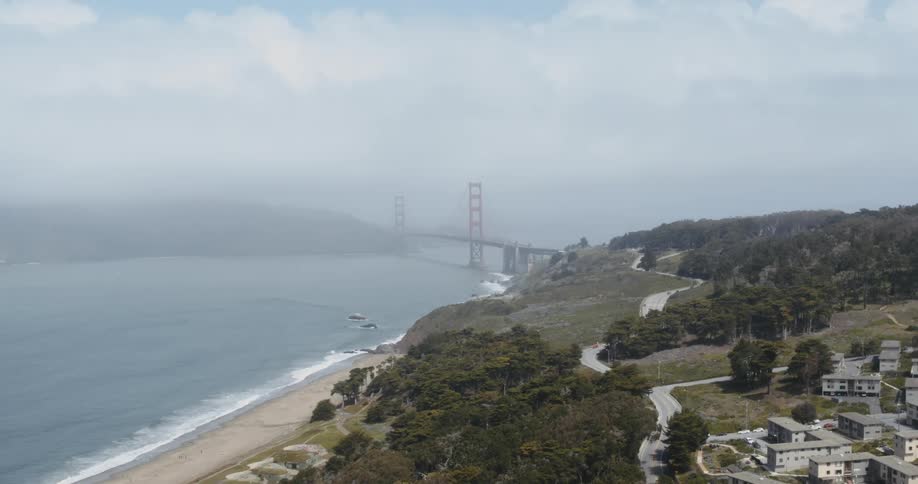 Two coastlines connected by a large bridge shrouded in fog during the day