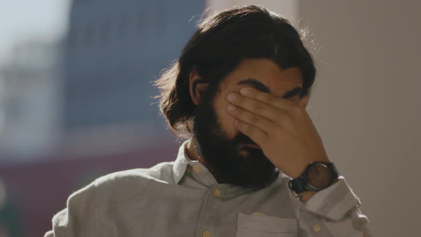 A sleep deprived business man looking at a screen takes off his glasses to rub eyes