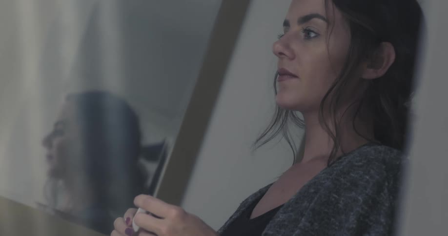 An apprehensive woman holding a pregnancy test stands in a bathroom while lost in thought