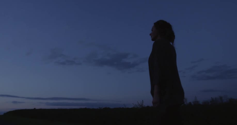 Woman walking around in the field is silhouetted against the sky at dusk