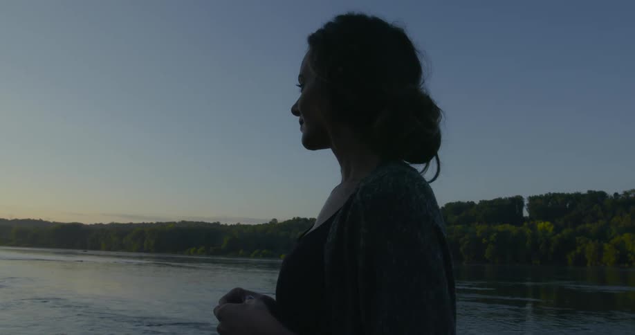 A woman stands on the shore and looks out at the water