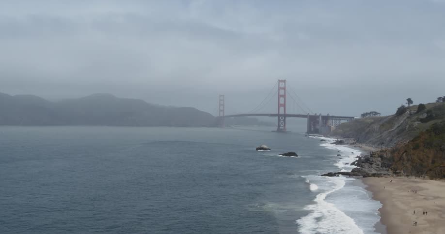 Aerial view of a suspension bridge covered in mist close to the coast next to the ocean