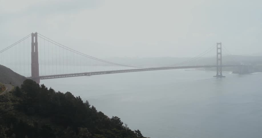 A road leads to a suspension bridge stretching across the water and into the fog on the other side