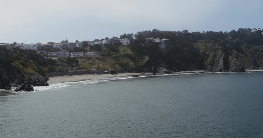 An aerial view of a lake with people on the beach and houses in a neighborhood behind the beach