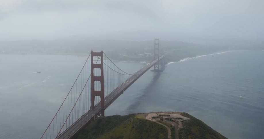 Aerial view of traffic driving over a suspension bridge covered in fog next to the ocean