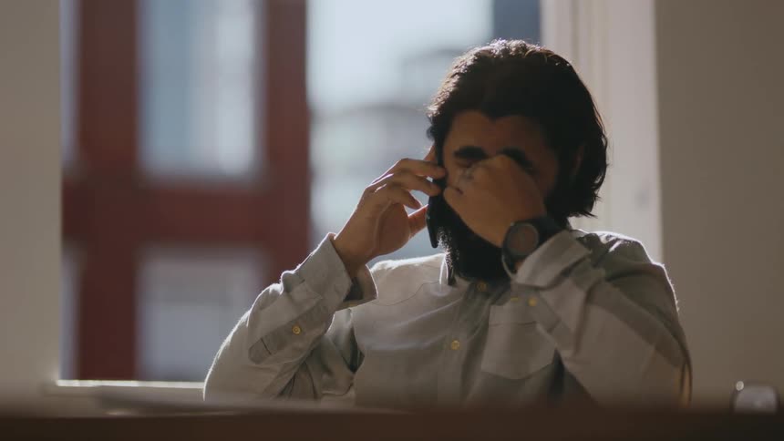 Young tired business man sitting at a desk talking on the cellphone