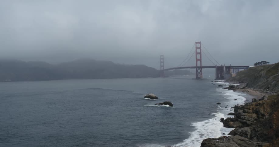 Waves crash against the foggy shore near the bridge