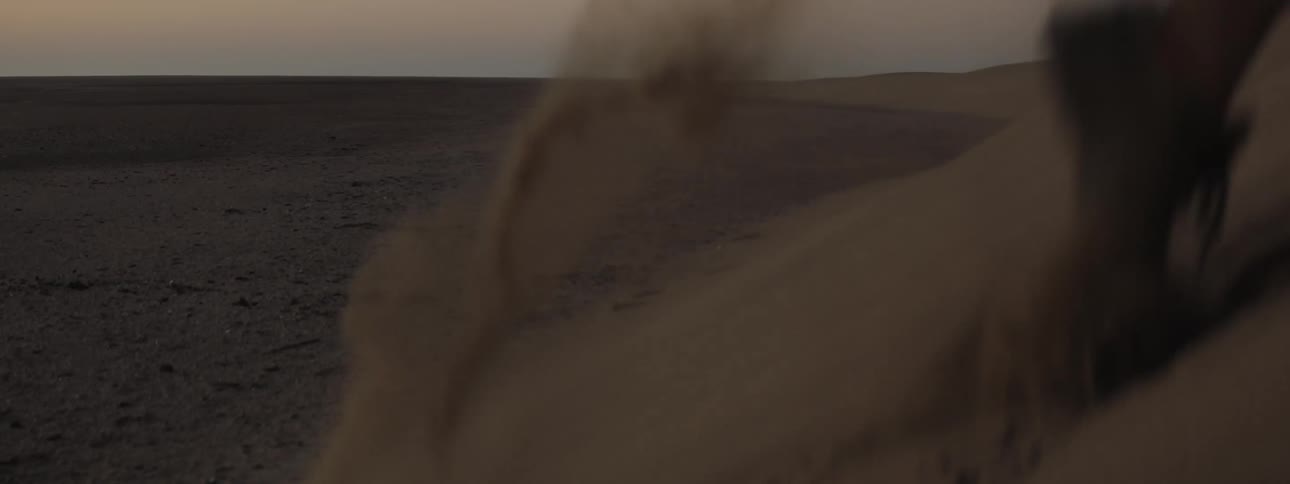 Close-up of a person jogging up a sand dune at dusk