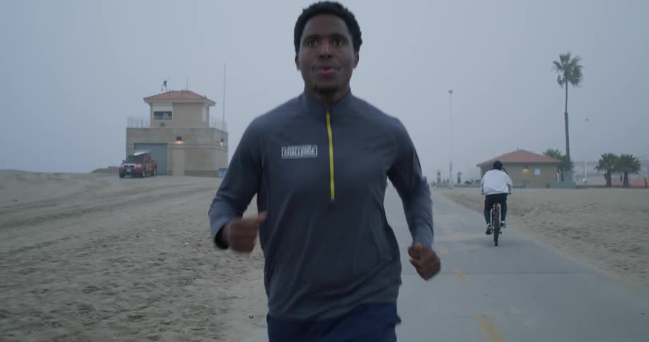 A man runs on a path by the beach as anothre person bikes past him