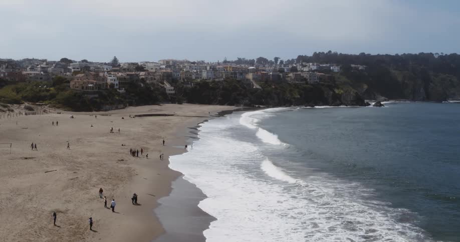 Aerial view of people walking on the sand of a beach near a small town next to the ocean