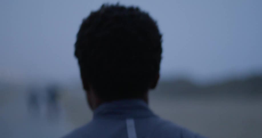 A mans head and shoulders bounce up and down as he jogs on a road