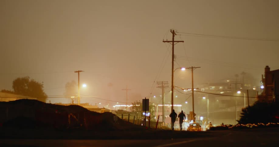 People run in pairs down a hilly neighborhood street as an ambulance with flashing lights passes by