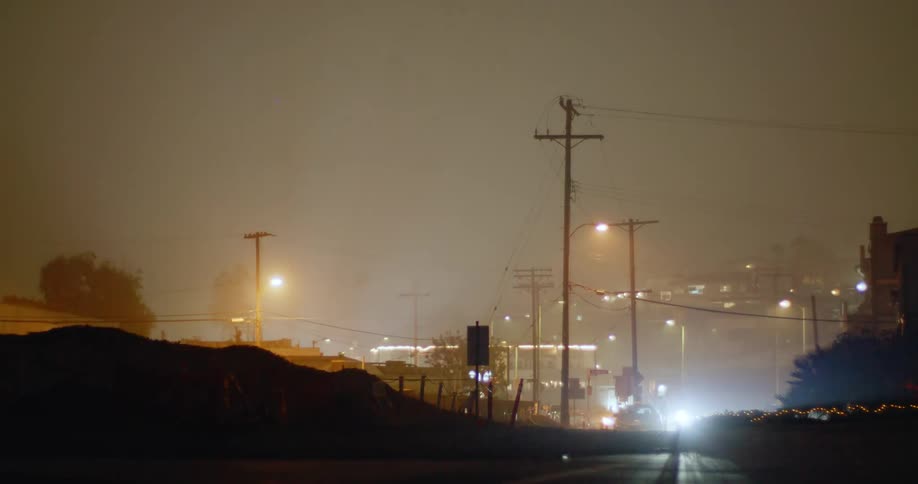 Strobing light from street lamps on the street of a small town covered in mist at night