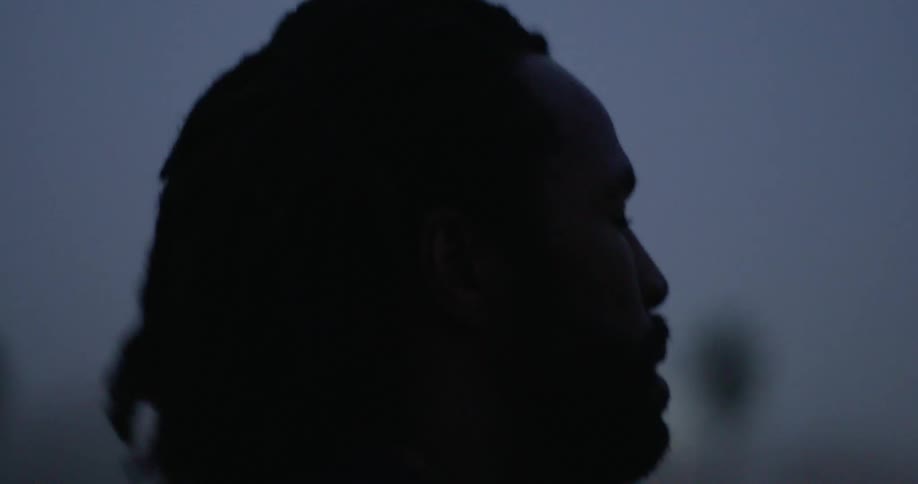A man hair dreads bounce up and down while he jogs outside at night