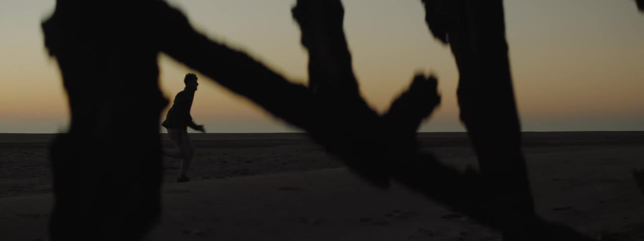 Silhouette of a man running near wreckage on a beach