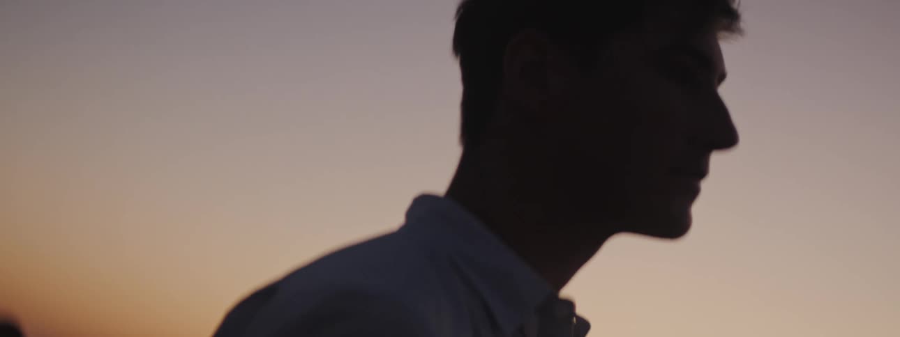 Man with blue shirt is silhouetted against the sky at dusk
