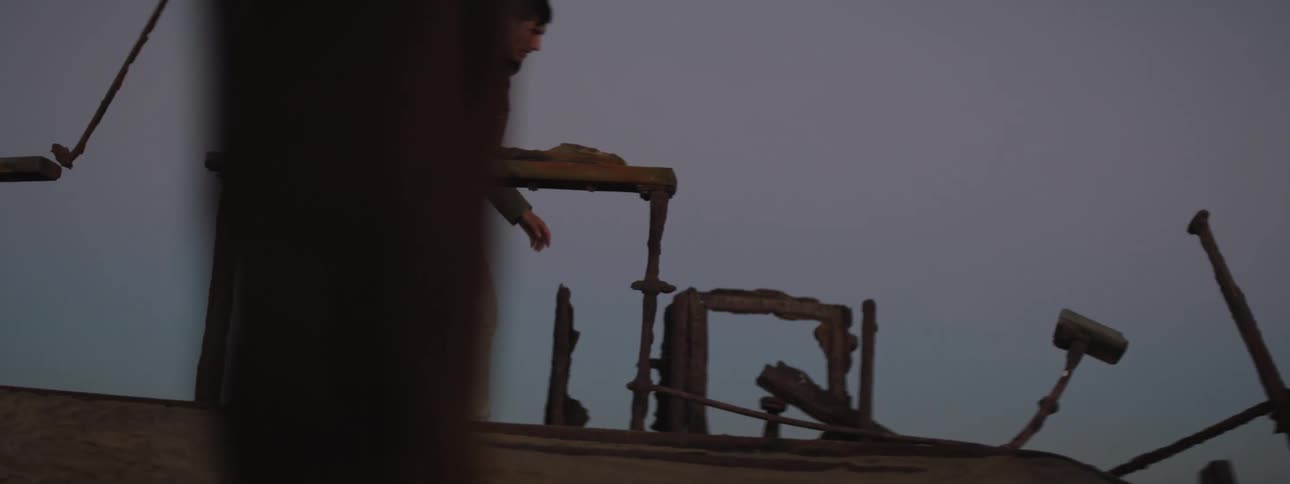 Young man walking through the rusted ruins of a shipwreck at evening