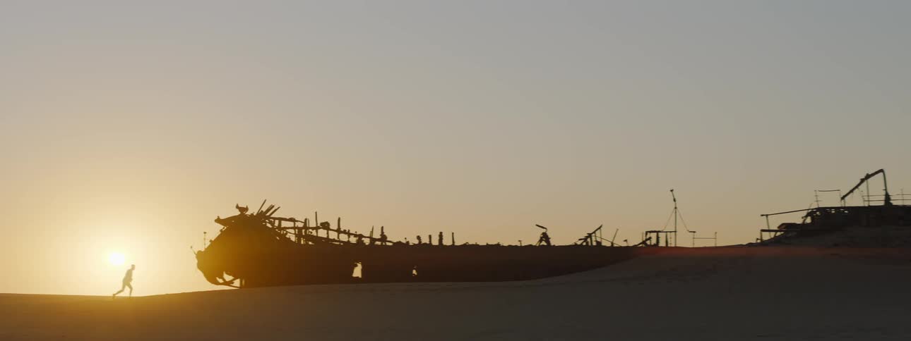 Silhouette of someone running near a shipwreck on a beach