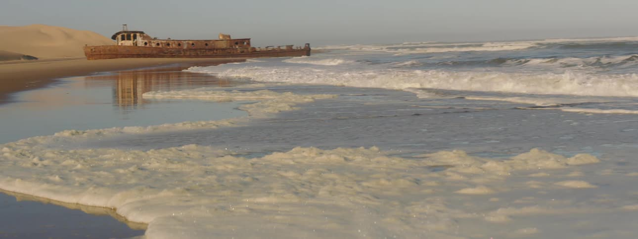 Waves rolling over a beach with old wrecked ship on shore