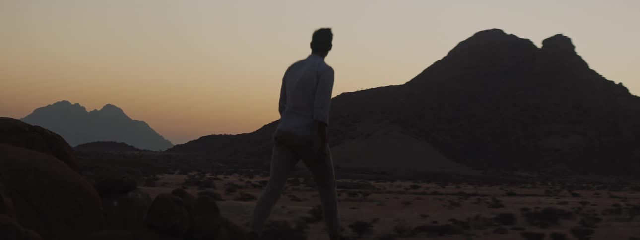 A man walking through desert region near mountains at dusk