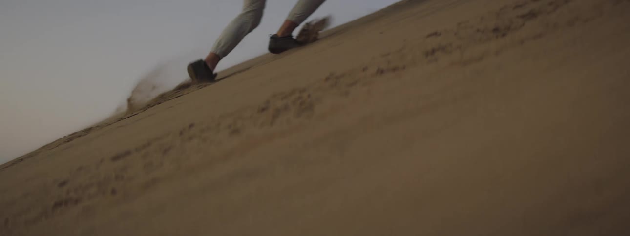 A man running up a sand dune and climbs on wreckage