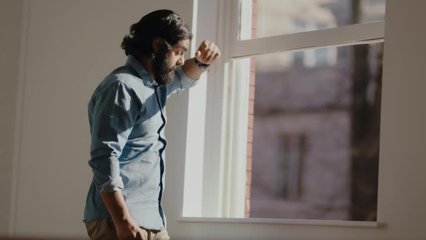 Tired man wearing glasses peers out a window