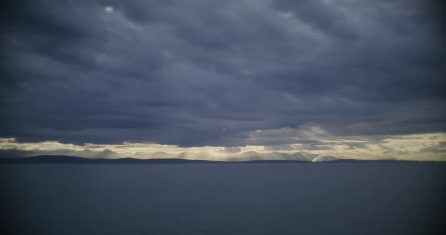 Dark clouds on an overcast sky hanging over the ocean with mountains in the horizon