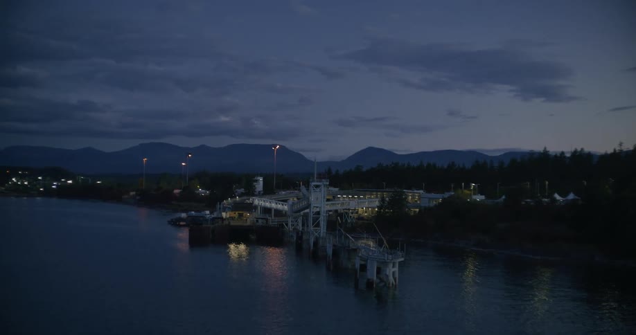 The silhouette of mountains behind a pier and dock with lights shimmering on the water surface