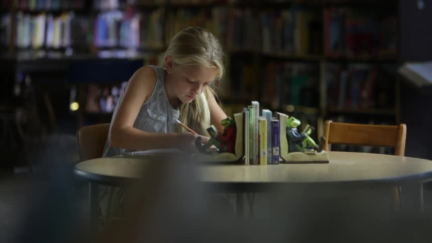 A girl is sitting at a table writing with a pencil
