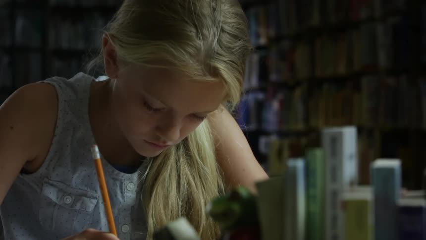 A girl with blonde hair writes with a pencil