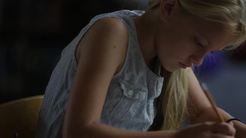 A girl is sitting at a table writing with a pencil