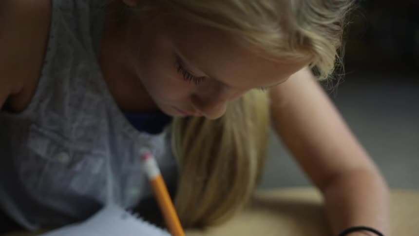 Girl sits at a table and writes with a pencil