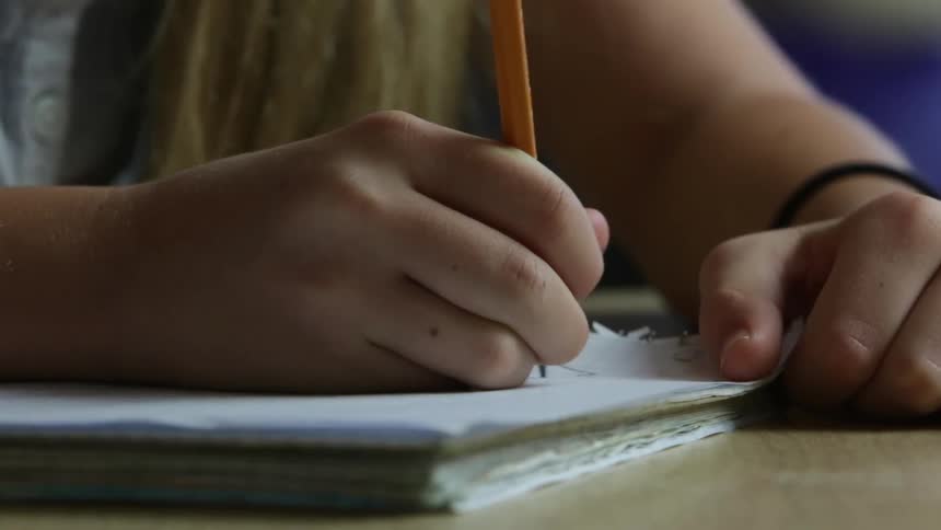 A girl is writing in a notebook with a pencil