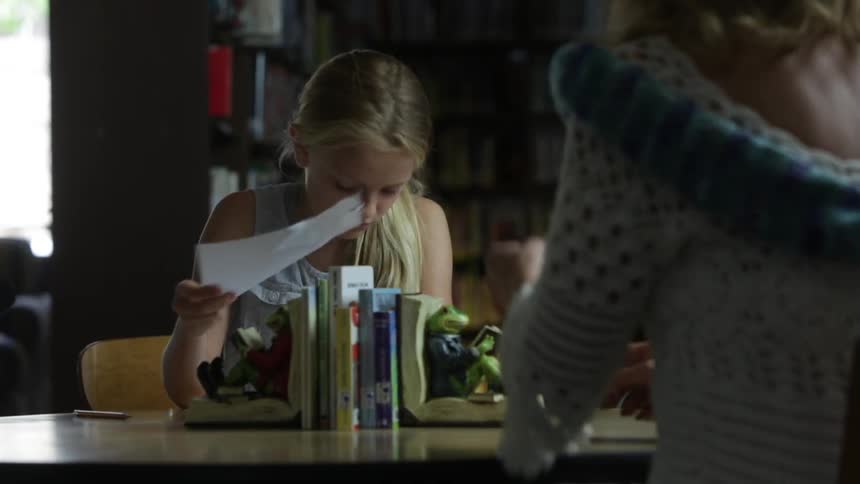 A girl rips a paper from a book and hands it to a woman
