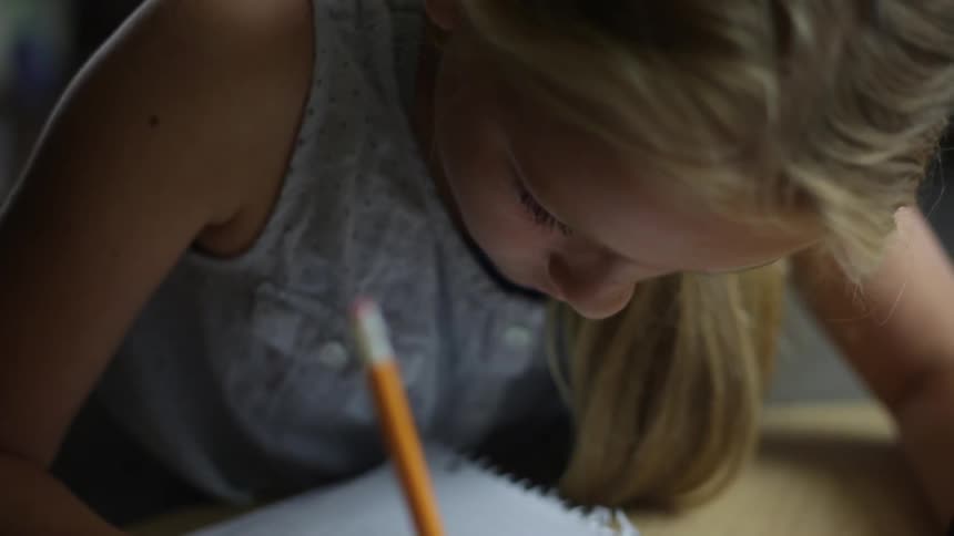 Girl writes on a notebook with a pencil