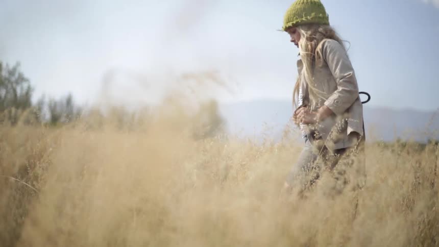 A girl walks through a field of tall yellow grass