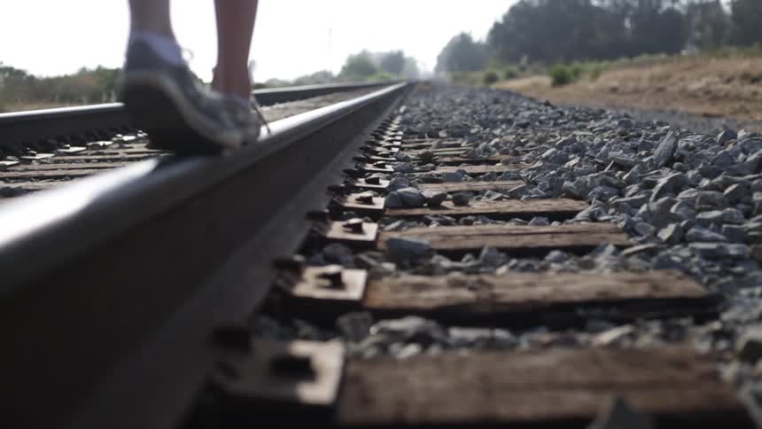 A person in tennis shoes walks across a railroad rail on a track