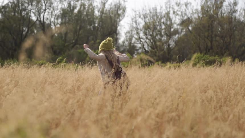 A girl is walking in tall yellow grass