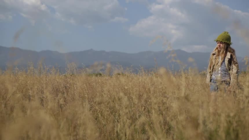 A girl walks in tall grass and picks up a stick