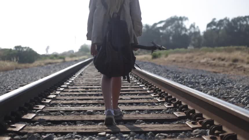 A girl holding a stick walks on the tracks