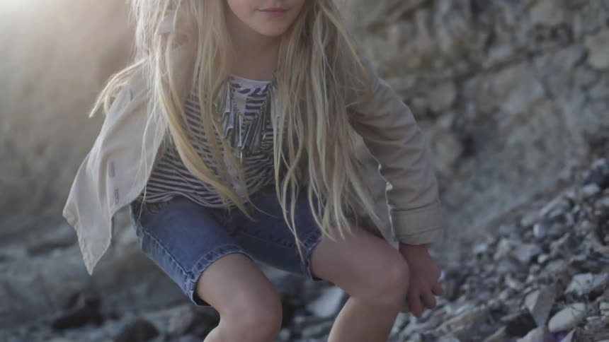 A girl picking up rocks near a cliff and placing them in her backpack