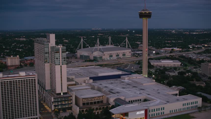 An aerial flyover of a metropolitan area contains several tall buildings and a remarkable tower with a spire