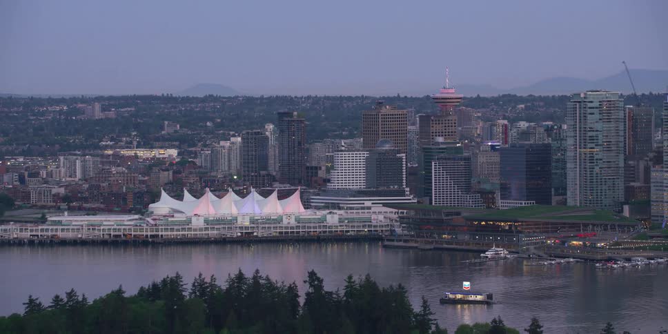 Conifer trees cover peninsula across from marina nestled near downtown skyscrapers on hazy day