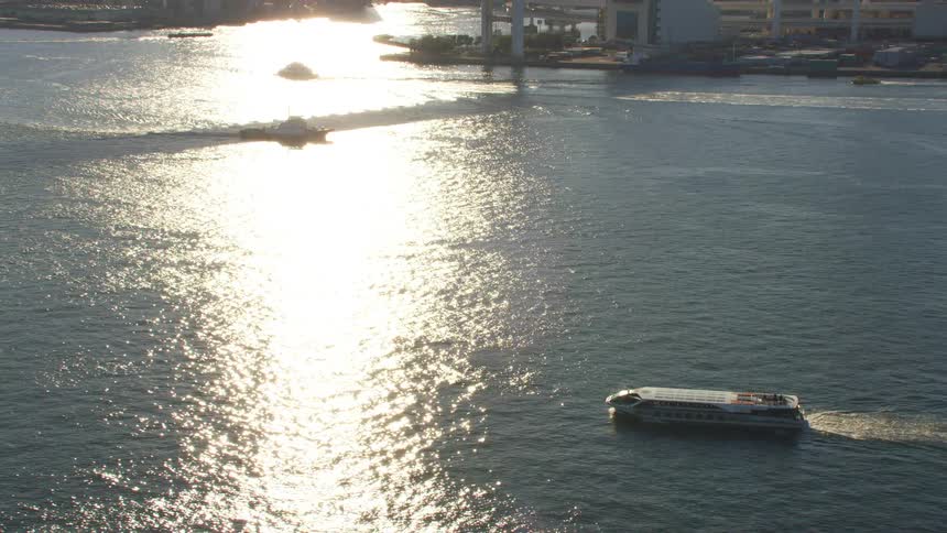 Cruise ship sails through sun glare reflecting from water with city in the background